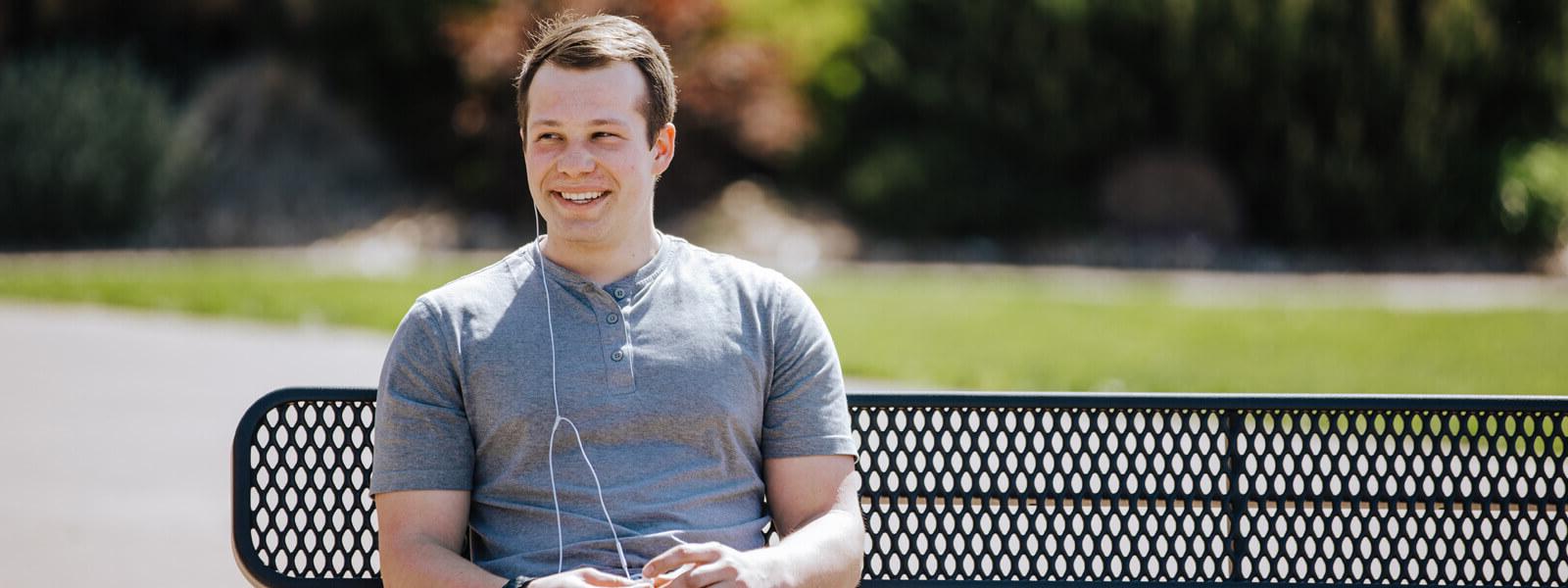 Male student sitting on bench with headphones smiling